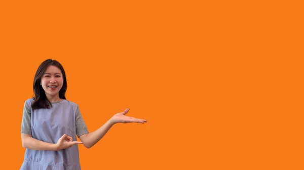 亚洲女人 手掌上握着一个虚构的复制空间 插入一个广告 显示复制空间指向 展示她的手在橙色背景下呈现的东西 — 图库照片