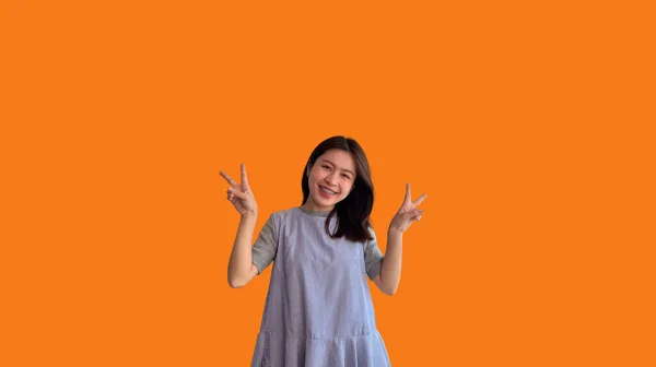 喜びと楽しさを示す2本の親指アップジェスチャーを作る若いアジアの女性 良い友情のシンボル 人気の写真ポーズ V字型の指を作る オレンジの背景 — ストック写真