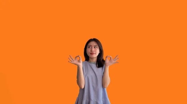 手でOk記号を行うオレンジの背景に若いアジアの女性 をシンボル ようこそ 指示通りに行う 注文に従う すべての条件の受諾 — ストック写真