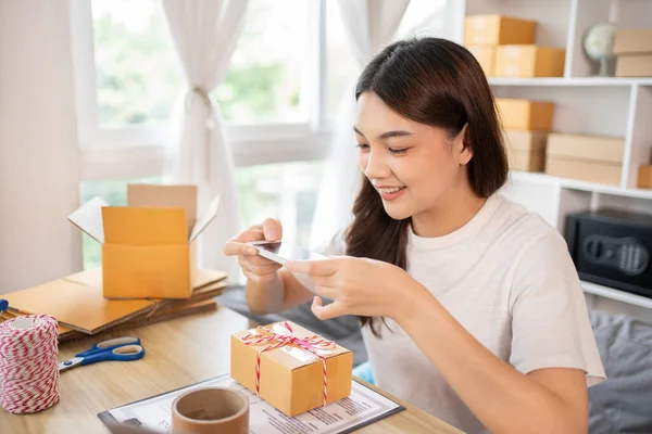 Asian Entrepreneur Working from Home, Capturing Identity Verification and Product Shipping on Mobile Phone, Working at Home: Online Store Management and Package Delivery for SMEs and Entrepreneurs.