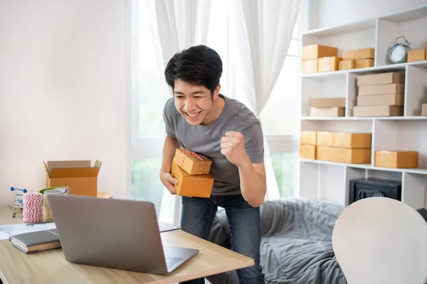 Happy man Celebrating Order from Internet Customer: New Business Style at Home, Online Selling, Young Entrepreneur\'s Success: Work-from-Home SME Owner Thrives in Online Sales, Packing Box.