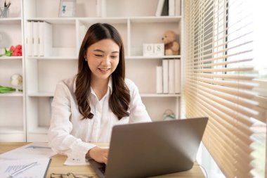Woman using laptop to work or do homework at home with smiling face in her office, Creating happiness at work with a smile, Live performance or vdo call with laptop, Work from home.