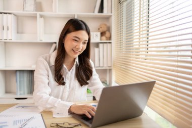 Woman using laptop to work or do homework at home with smiling face in her office, Creating happiness at work with a smile, Live performance or vdo call with laptop, Work from home.