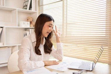 Woman using laptop to work or do homework at home with smiling face in her office, Creating happiness at work with a smile, Live performance or vdo call with laptop, Work from home.