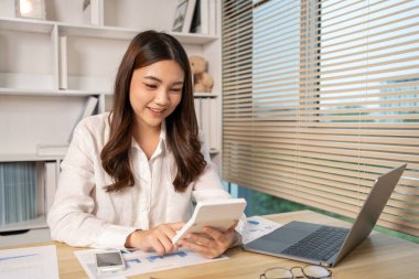 Evde çalışan Asyalı kadın, evin gelirini hesaplamak için hesap makinesine basın - evin giderlerini hesaplamak ve bilgiyi kaydetmek ve doğruluğunu kontrol etmek için dizüstü bilgisayarı kullanın..
