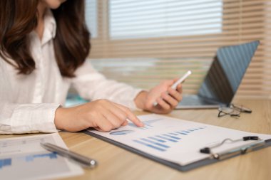 Asyalı kadın çalışan telefonda konuşuyor ve laptopta gülümseyen yüzüyle çalışıyor, ofis çalışanları çalışıyor ve telefon konuşmaları, hatırlatıcı notlar alıyor, telefonda iş konuşmaları yapıyor..