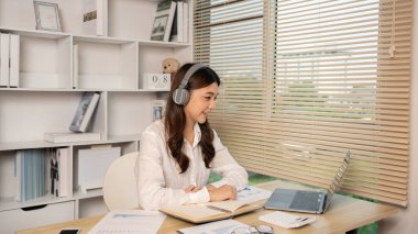 Woman using laptop to work or do homework at home with smiling face in her office, Creating happiness at work with a smile, Live performance or vdo call with laptop, Work from home.