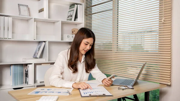 Asyalı kadın çalışan telefonda konuşuyor ve laptopta gülümseyen yüzüyle çalışıyor, ofis çalışanları çalışıyor ve telefon konuşmaları, hatırlatıcı notlar alıyor, telefonda iş konuşmaları yapıyor..