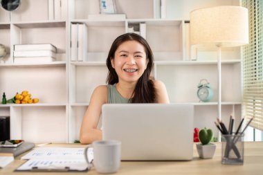 Woman using laptop to work or do homework at home with smiling face in her office, Creating happiness at work with a smile, Live performance or vdo call with laptop, Work from home.