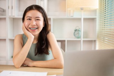 Woman using laptop to work or do homework at home with smiling face in her office, Creating happiness at work with a smile, Live performance or vdo call with laptop, Work from home.