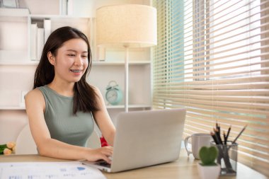 Woman using laptop to work or do homework at home with smiling face in her office, Creating happiness at work with a smile, Live performance or vdo call with laptop, Work from home.