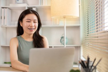 Woman using laptop to work or do homework at home with smiling face in her office, Creating happiness at work with a smile, Live performance or vdo call with laptop, Work from home.