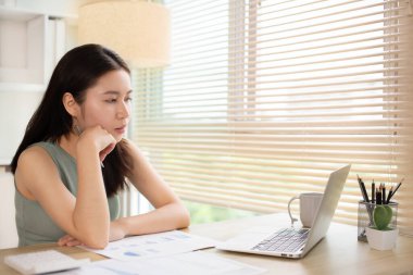 Woman using laptop to work or do homework at home with smiling face in her office, Creating happiness at work with a smile, Live performance or vdo call with laptop, Work from home.