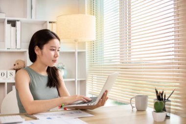 Woman using laptop to work or do homework at home with smiling face in her office, Creating happiness at work with a smile, Live performance or vdo call with laptop, Work from home.