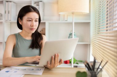 Woman using laptop to work or do homework at home with smiling face in her office, Creating happiness at work with a smile, Live performance or vdo call with laptop, Work from home.