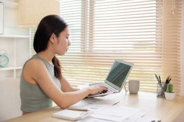 Woman using laptop to work or do homework at home with smiling face in her office, Creating happiness at work with a smile, Live performance or vdo call with laptop, Work from home.