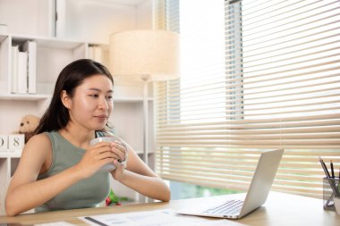 Woman using laptop to work or do homework at home with smiling face in her office, Creating happiness at work with a smile, Live performance or vdo call with laptop, Work from home.