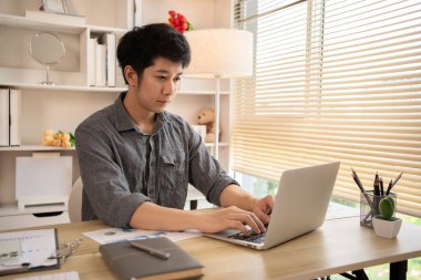 Adam ofisteki dizüstü bilgisayarında oturmuş yüzünde kararlı bir ifadeyle ev konforuyla çalışıyor, erkek eli dizüstü bilgisayara basıyor, evden çalışıyor..