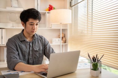 Adam ofisteki dizüstü bilgisayarında oturmuş yüzünde kararlı bir ifadeyle ev konforuyla çalışıyor, erkek eli dizüstü bilgisayara basıyor, evden çalışıyor..