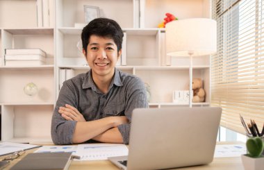 Yakışıklı genç adam, elinde laptop ve ofis ekipmanıyla masa başında oturuyor ve hafta başında çalışmaya hazır gülümsüyor. Üretken Çalışma Haftasına Pozitif Başlangıç.