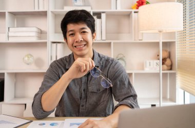 Yakışıklı genç adam, elinde laptop ve ofis ekipmanıyla masa başında oturuyor ve hafta başında çalışmaya hazır gülümsüyor. Üretken Çalışma Haftasına Pozitif Başlangıç.