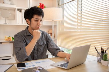 Yakışıklı genç adam, elinde laptop ve ofis ekipmanıyla masa başında oturuyor ve hafta başında çalışmaya hazır gülümsüyor. Üretken Çalışma Haftasına Pozitif Başlangıç.