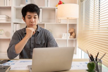 Yakışıklı genç adam, elinde laptop ve ofis ekipmanıyla masa başında oturuyor ve hafta başında çalışmaya hazır gülümsüyor. Üretken Çalışma Haftasına Pozitif Başlangıç.