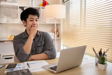 Yakışıklı genç adam, elinde laptop ve ofis ekipmanıyla masa başında oturuyor ve hafta başında çalışmaya hazır gülümsüyor. Üretken Çalışma Haftasına Pozitif Başlangıç.