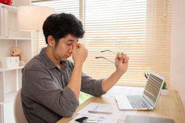 Yorgun genç adam gözlerini uzun ekran süresinden dinlendiriyor, göz yorgunluğu ve stres atağı, göz yorgunluğu semptomları, iş yorgunluğu, Dijital Göz Gerilimi.