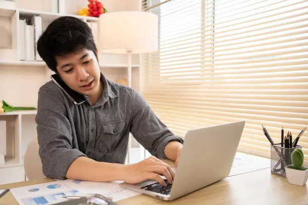 Genç Adam Çoklu Görev: Ev Ofisi 'nde dizüstü bilgisayarda yazmak ve telefonda konuşmak, çok işi olan ve işiyle çok meşgul olan genç bir adam.