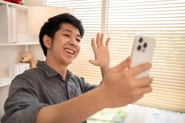Young Asian man greets his friends and colleague in a live video with a smile on his face, Online communication , Vdo call via phone, Social distancing, Internet learning.