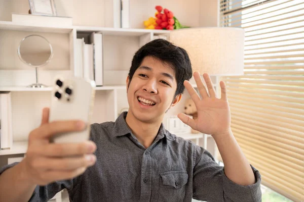 Young Asian man greets his friends and colleague in a live video with a smile on his face, Online communication , Vdo call via phone, Social distancing, Internet learning.