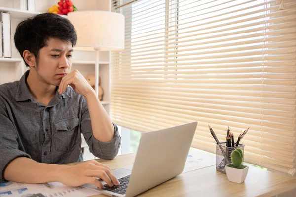 Yakışıklı genç adam, elinde laptop ve ofis ekipmanıyla masa başında oturuyor ve hafta başında çalışmaya hazır gülümsüyor. Üretken Çalışma Haftasına Pozitif Başlangıç.