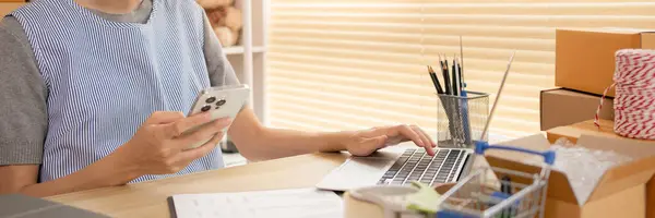 Sell products online, Woman Multitasking: Typing on Laptop and Send a message on your mobile phone at Home Office, Home Workspace, A lot of work and is very busy with work, Freelance working.