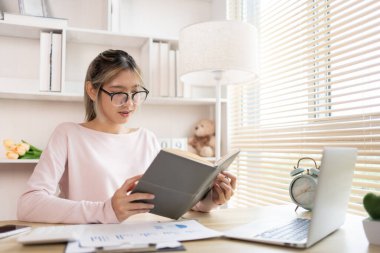 Kitap okuyan bir kadın, özel bir ofiste kitap okuyan bir öğrenci, kişisel çalışma, kitaplardan ders kitapları, daha fazla bilgi edinin, ofiste masanın üzerine yerleştirilmiş bir bilgisayar ya da dizüstü bilgisayar var,.