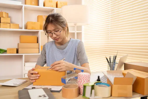 Sell products online, Woman is writing down the customer\'s details and addresses on box in order to prepare for shipping according to the information, Packing box, Sell online.
