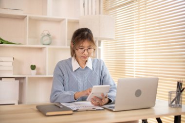 Dizüstü bilgisayarın önünde çalışan bir kadın, emlak, finans, muhasebe, tex, ev için çalışmanın istatistiksel grafiklerini gösteren bir hesap makinesi basıyor..