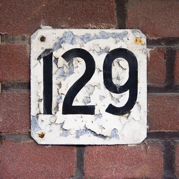 Yaşlı, çatırdayan ev numarası 129. Beyaz tabakta siyah harfler var.