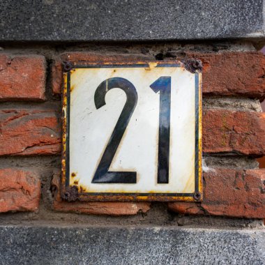 Kırmızı tuğlalı bir duvarda 21 numaralı paslı, mayalı ev.