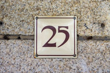 '25' (25) yazılı, doğal bir taş duvara sabitlenmiş bir ev numarası..