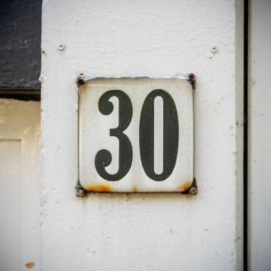 n emelli ev numarası '30' (30), bir kapı çerçevesine sabitlenmiş.
