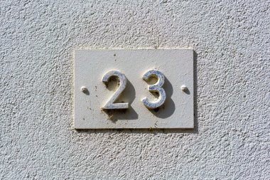 '23' yazan kabartmalı beyaz bir ev numarası, beyaz bir duvara monte edilmiş bir plakette..