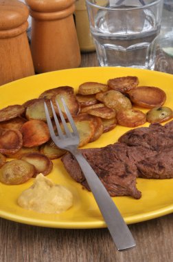 Patatesli biftek ve çatalla servis edilen hardal.