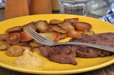 Patatesli biftek ve çatalla servis edilen hardal.