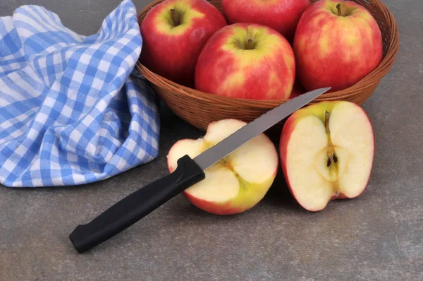 Apple cut in half with a knife with a basket of apples in the background