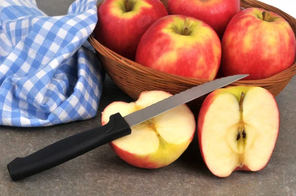 Apple cut in half with a knife with a basket of apples in the background