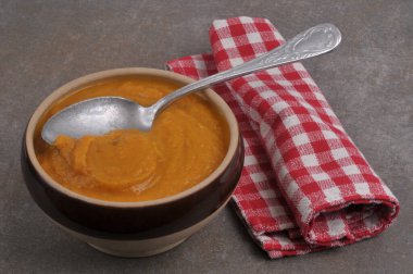 Bir kase havuç çorbası, bir kaşık ve arka planda yakın plan bir peçete. 