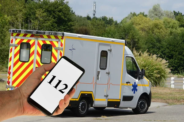 救急車を背景に携帯電話に表示される緊急番号 — ストック写真