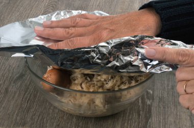 Birisi alüminyum folyoyla bir kase yiyecek paketliyor. 