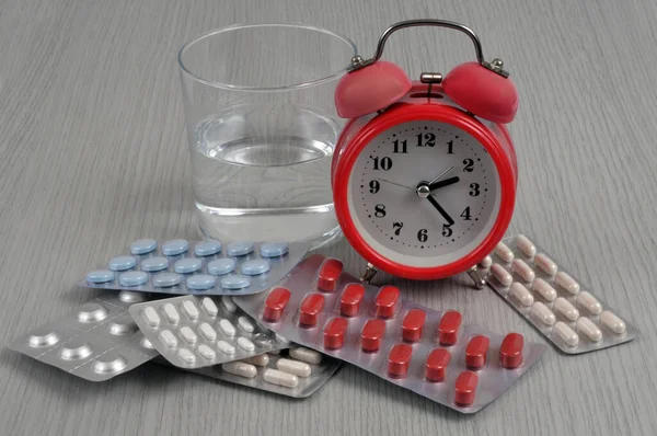 Medicine blister packs with an alarm clock and a glass of water